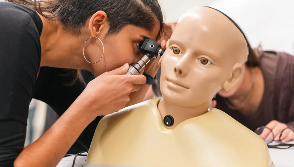A nursing student practices using an otoscope on a patient simulator