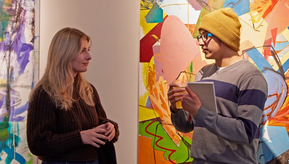 U N E students talk in front of two large colorful paintings in U N E's Portland Art Gallery