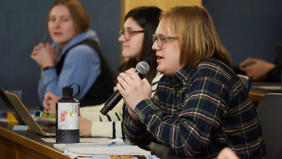 A U N E student holds a microphone as they ask a question from the audience of a C G H lecture