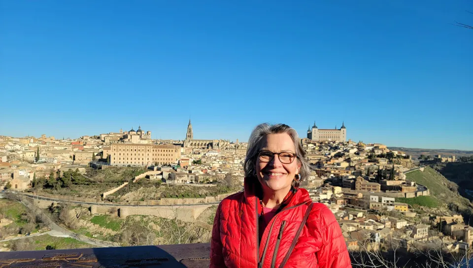 A woman smles for a photo in front of a countryside Spanish city