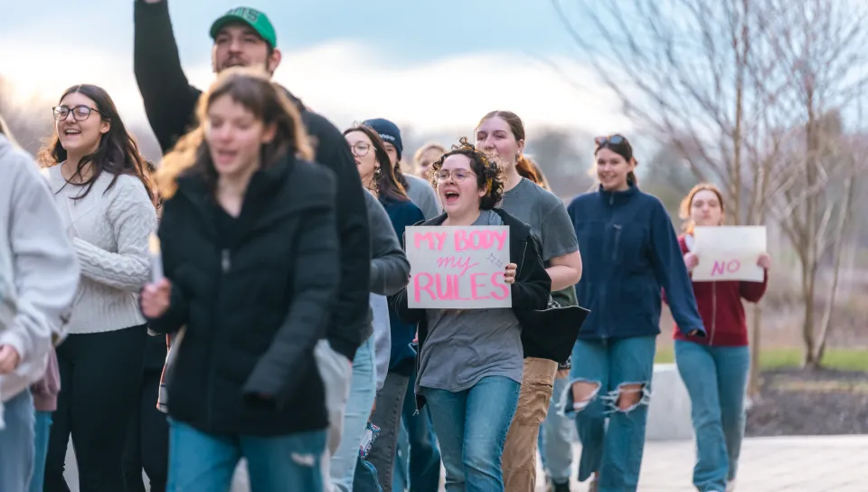 Students march on campus; a sign reads "My Body, My Rules"