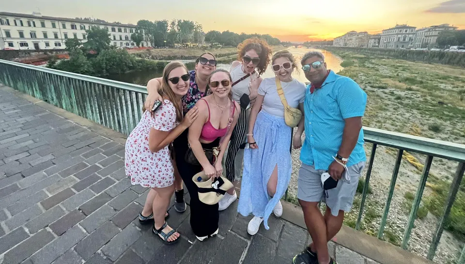 A group of U N E students and their professor stand in front of a sunrise