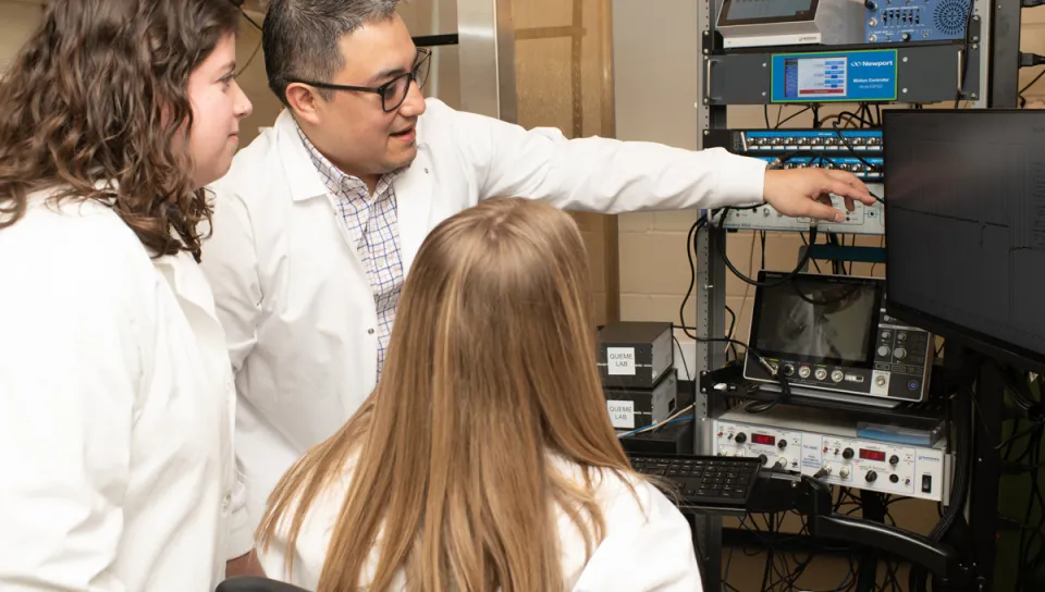 Luis Queme and two students look at a graph on a monitor in his lab