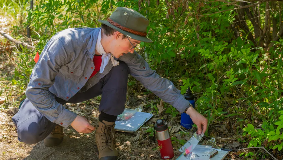 A U N E student picks up a plastic bag containing an artifact found at a dig site