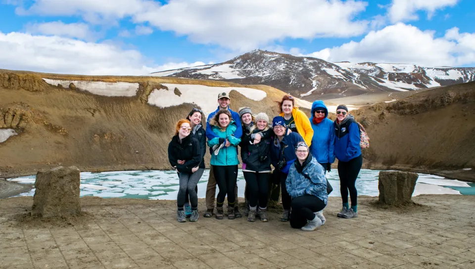 A group of students in winter gear stand in front of a crater filled with frozen glacier water