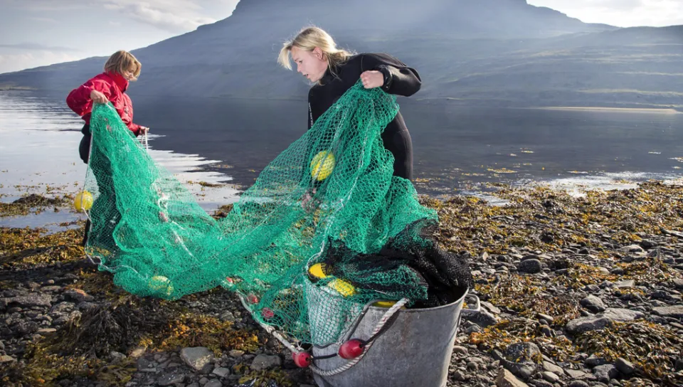 Two students remove a fishing net from the ocean off a rocky coastline