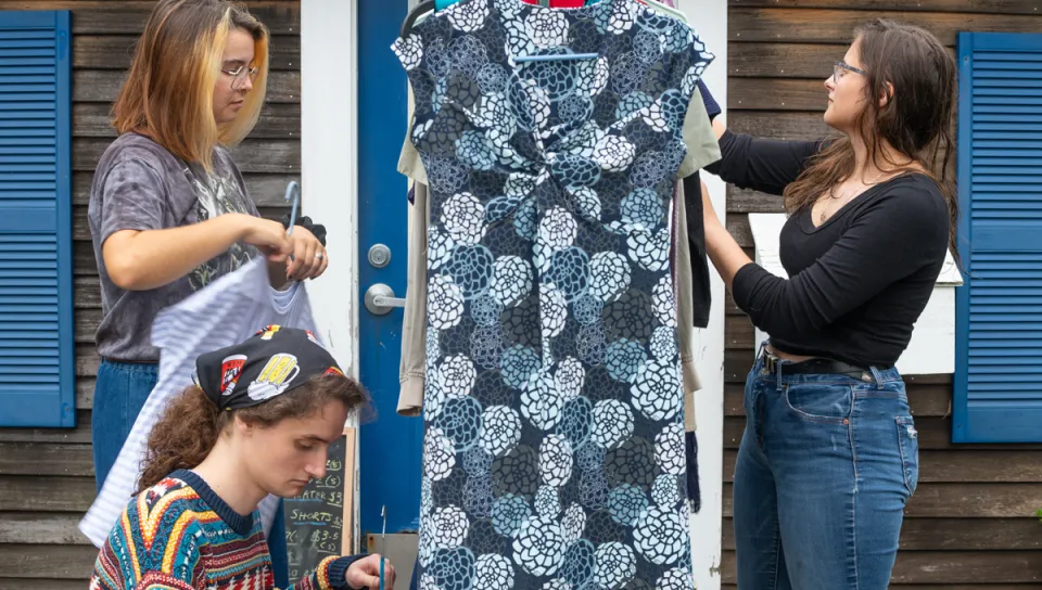 Three U N E students peruse a rack of clothing