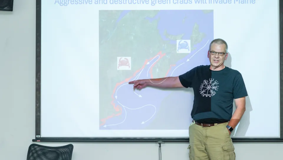 UNE's Markus Frederich points to a map on a slideshow presentation