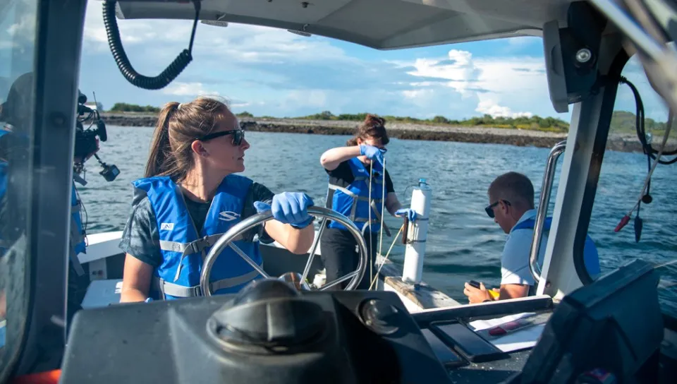 A U N E student wearing a blue life vest drives a boat in the ocean