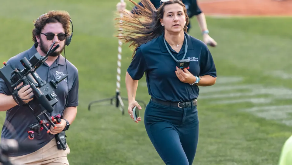 Morgan White runs across the baseball field while managing the team's mascot