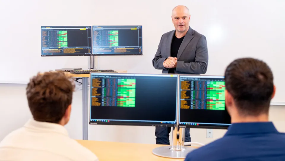 Two business students listen to a professor during a computer lab