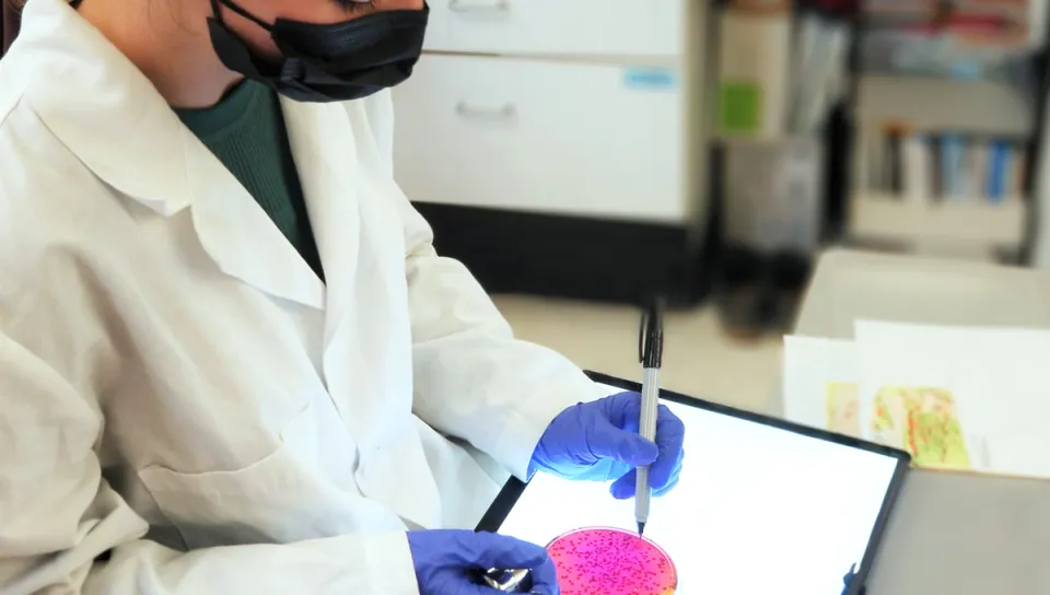 A student in a white lab coat marks a petri dish with a permanent marker