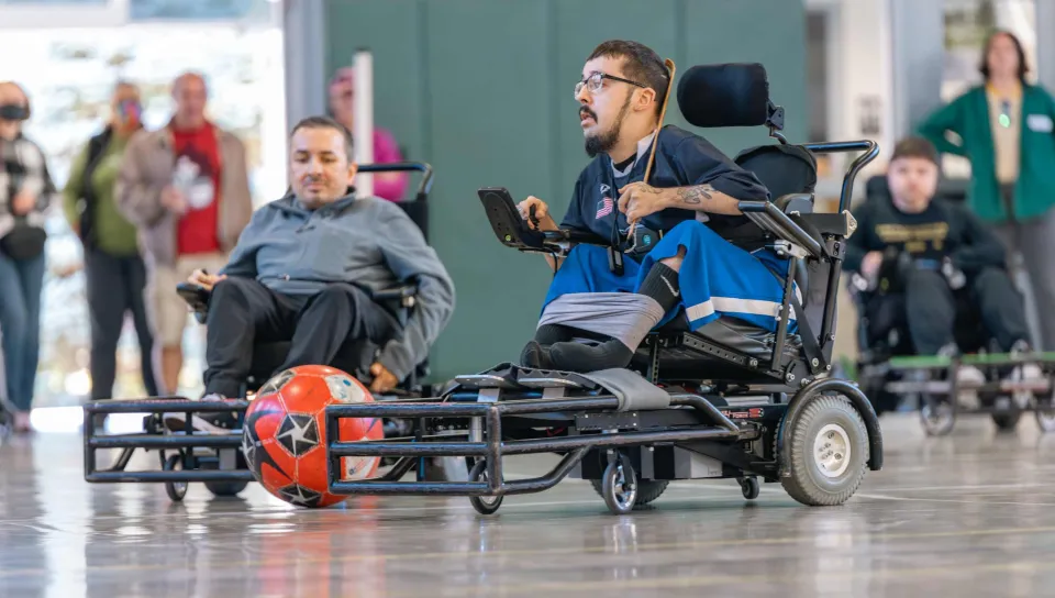 A man uses a power wheelchair to move a soccer ball