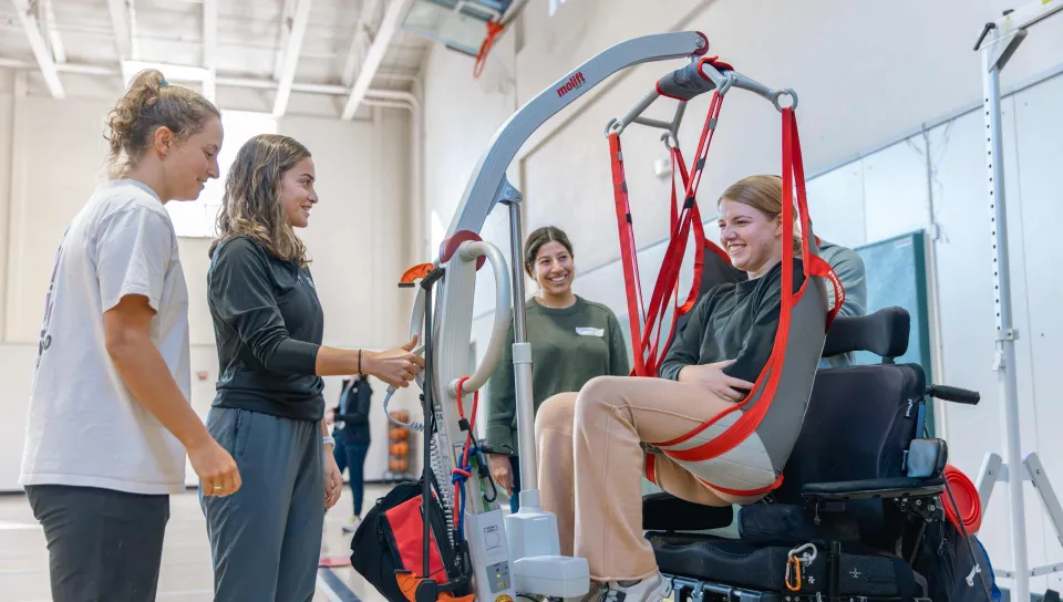 UNE students help a wheelchair user into a power wheelchair using ropes