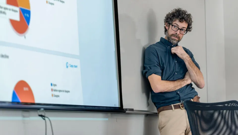 A UNE professor stands against a whiteboard while another professor speaks