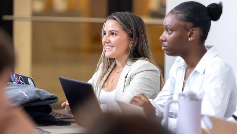 Two women business students work on their laptops
