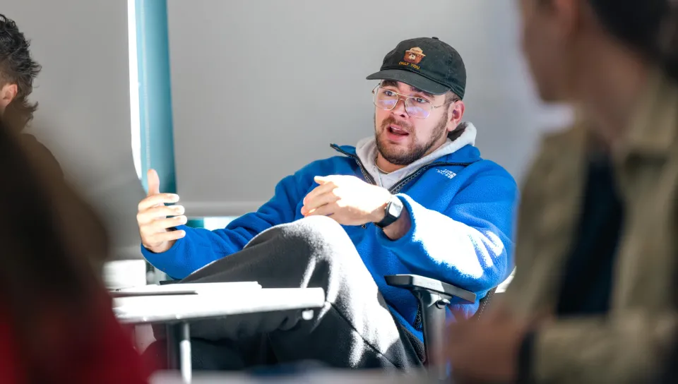 A student speaks during class from the back of the classroom