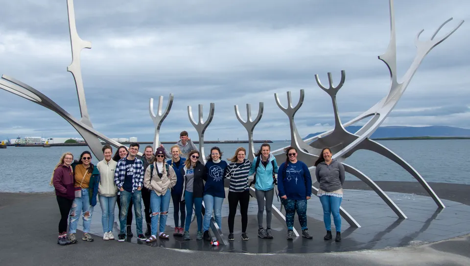 A group of U N E students pose in front of a steel art sculpture of a viking ship