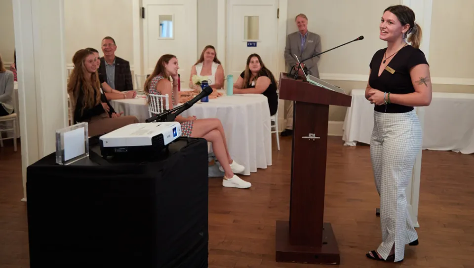 A Sustainability Fellow speaks to a small crowd from a podium