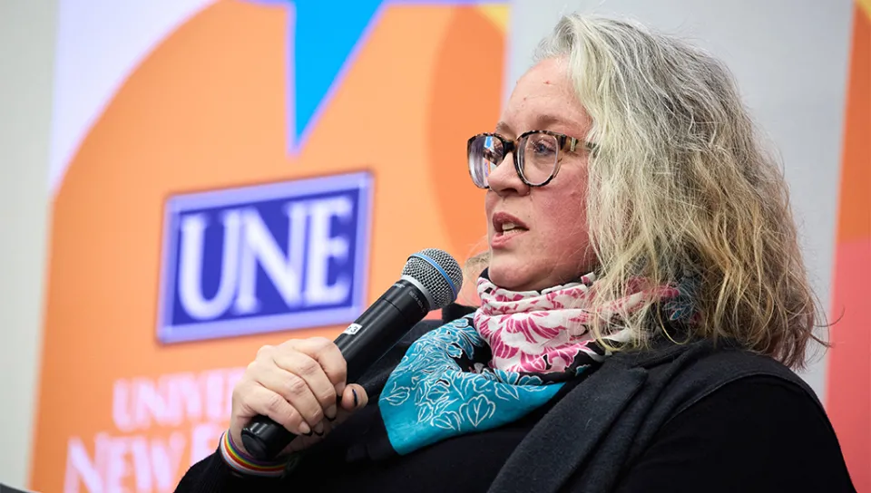 Shannon Zlotkowski speaks into a microphone and moderating the event