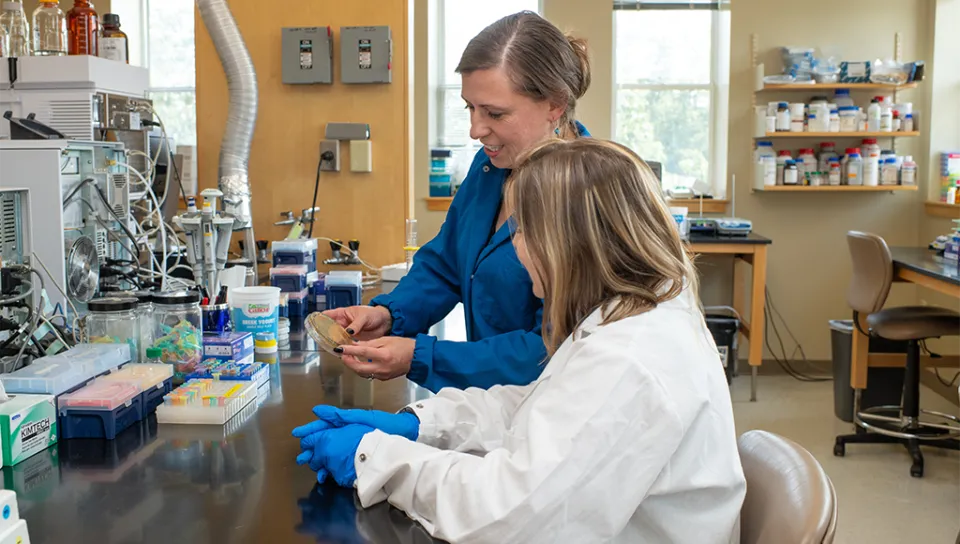 Eva Rose Balog holds a petri dish while a UNE student observes in the lab.