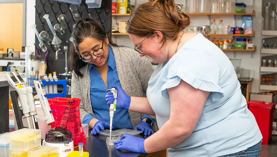Jennifer Garcia works with a UNE Student who pipets in the lab