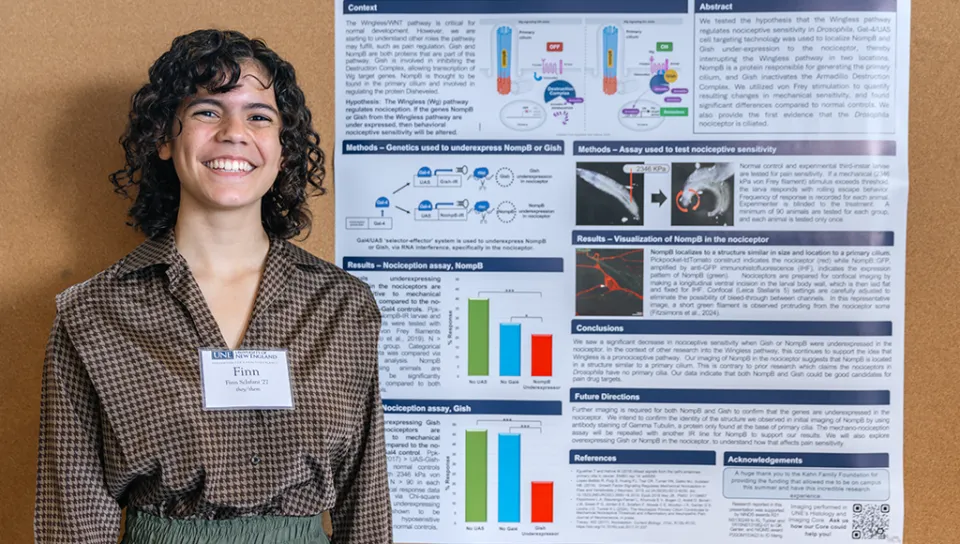 U N E student Finn Sclafani stands in front of a research poster and smiles at the camera