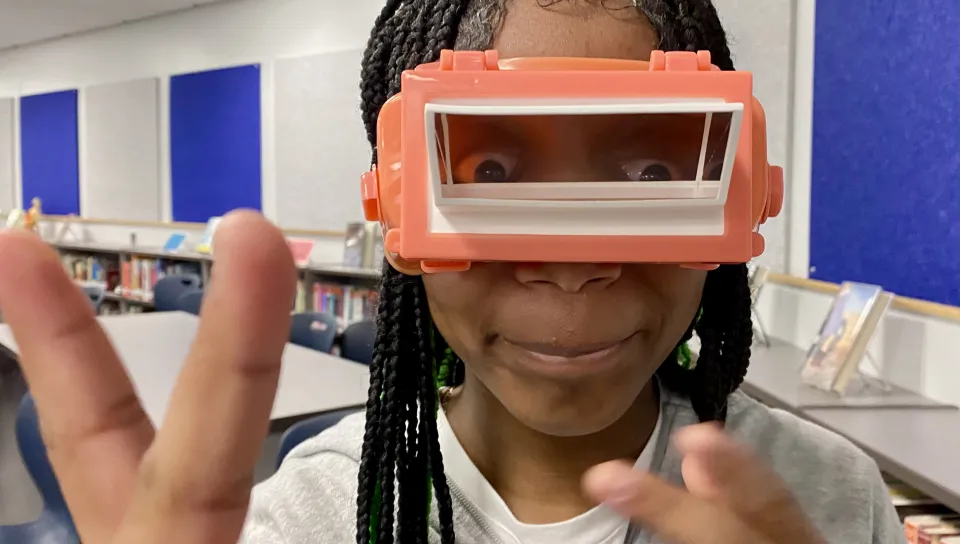 A student makes a "peace" sign while wearing vision-shifting goggles