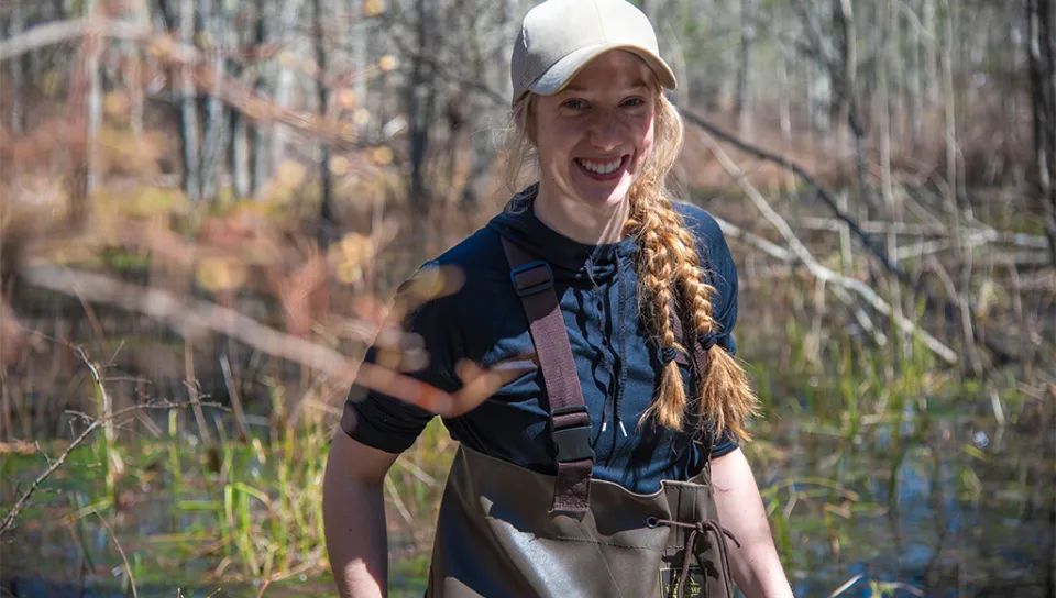 A student in waders walks through a vernal pool in a Maine forest