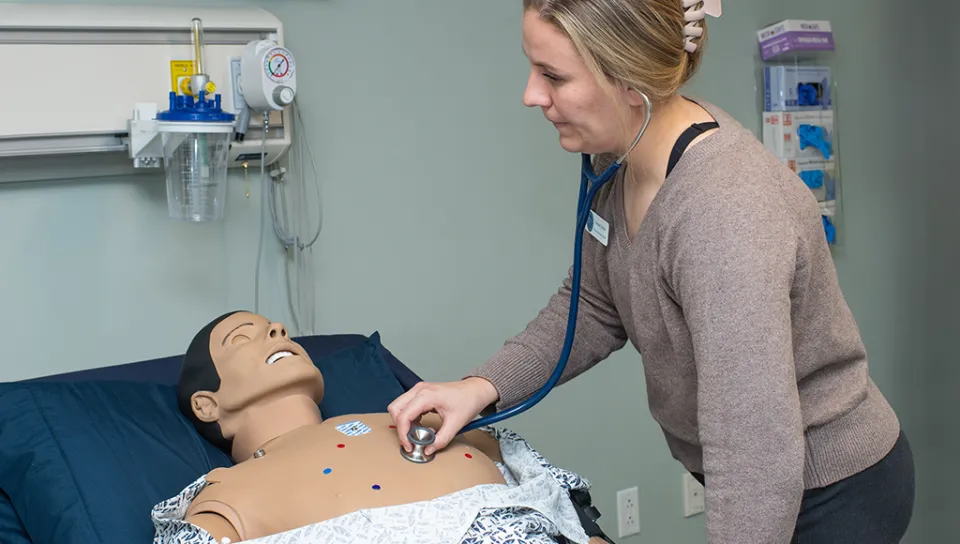 A health student listens to the heartbeat of a patient simulator