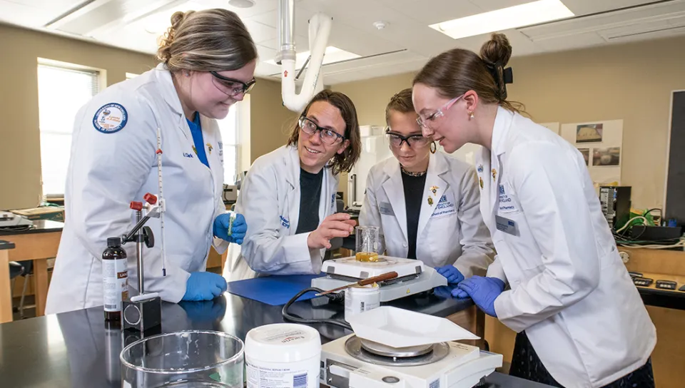 A group of four students weigh a beaker filled with a liquid during a compounding lab