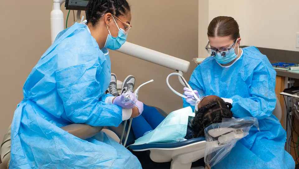 Two dental medicine students in blue scrubs check a childt's teeth in the Oral Health Center