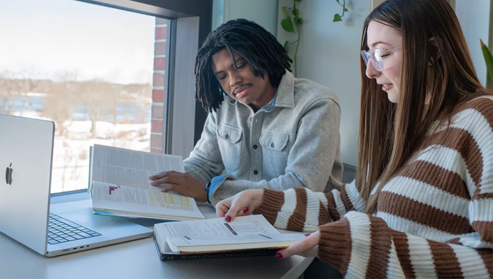 Two students read a textbook together in a room overlooking Biddeford Campus