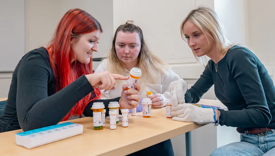 Three Gerontology students partake in a medication management activity in class