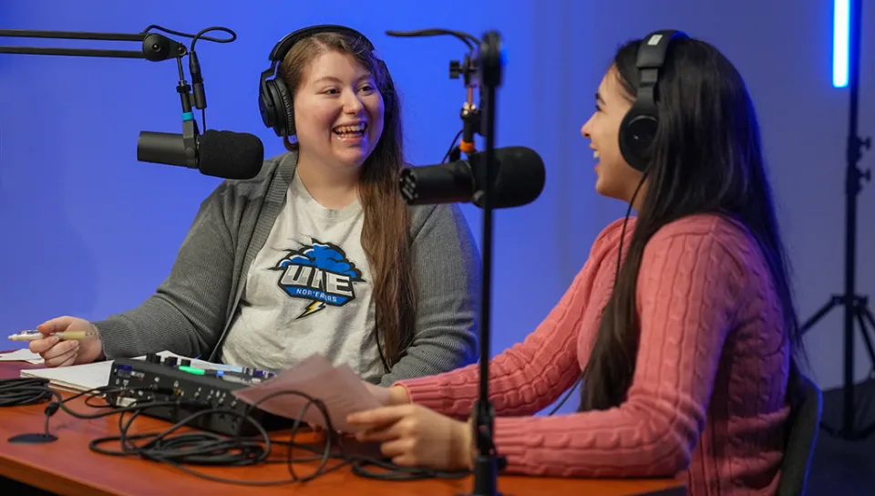Two students chat in front of microphones as they record a podcast
