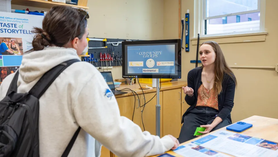 A student discusses her project, the 2025 UNE Story Slam, with an audience member