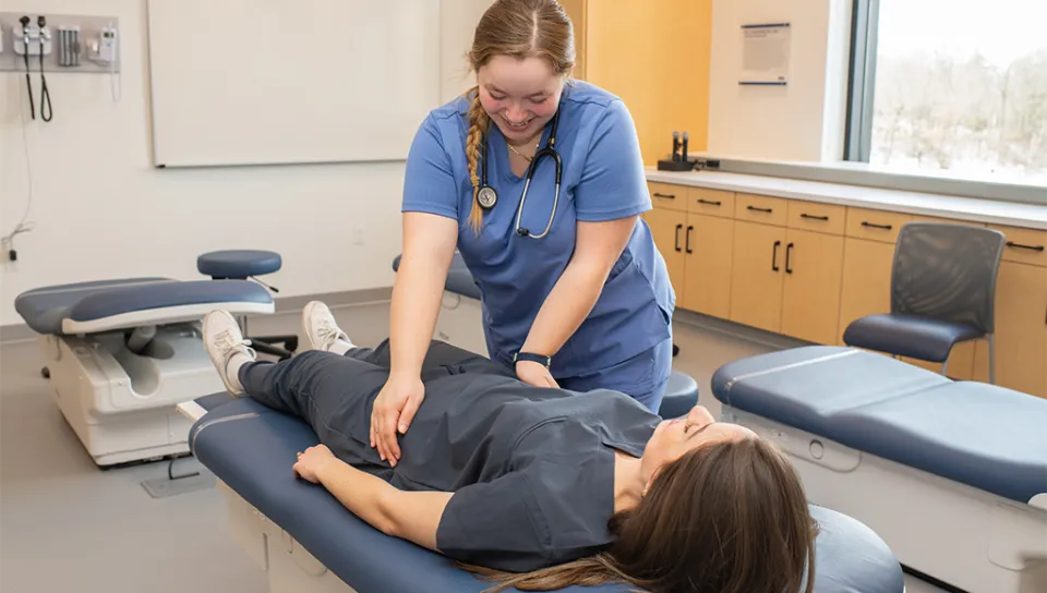 A health student practices doing an exam on another student laying on an examination table