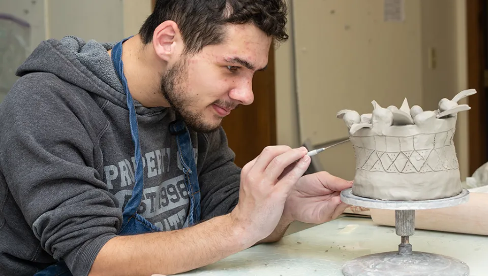 A student refines their unfired pottery
