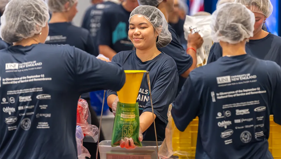 Several student volunteers in hair caps and matching t-shirts package food for Meals for Maine