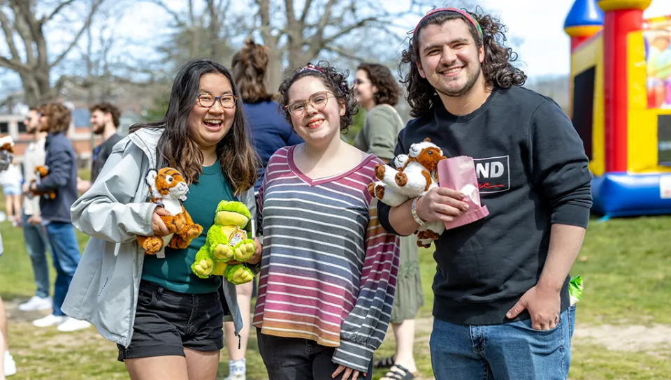 Three students holding stuffed animals smile for the camera at an on-campus carnival