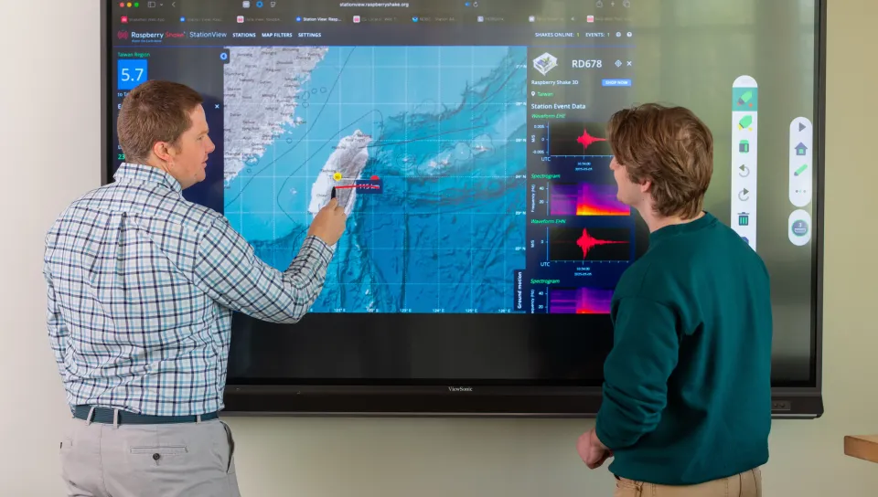 UNE Professor Will Kochtitzky displays a seismic activity map with a student