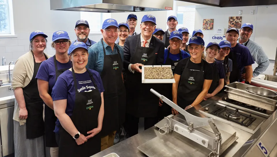 President Herbert stands with a group of U N E employees and students while holding up a fresh seaweed bar in the student kitchen