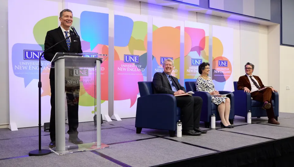 UNE President James Herbert introduces two panelists and a moderator onstage