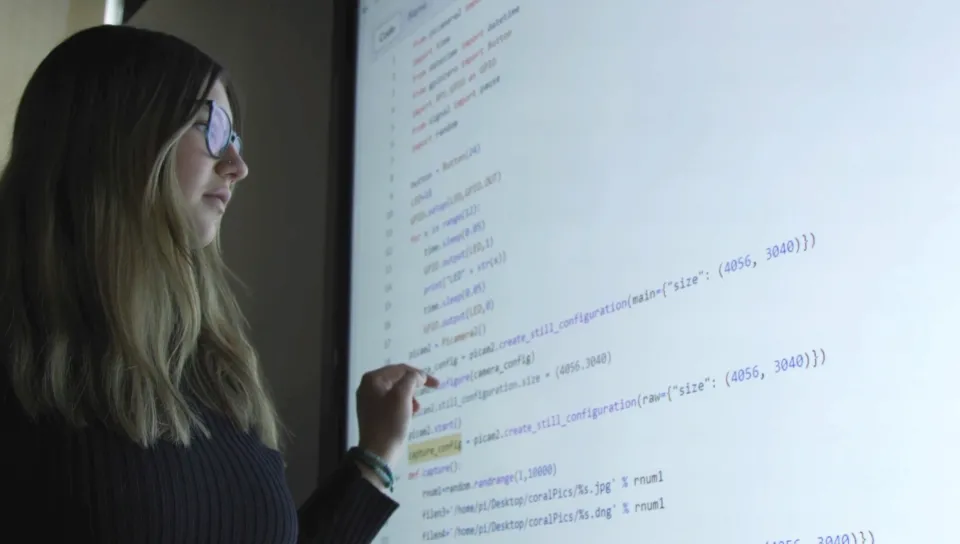 A computer science student reviews computer code on a large screen