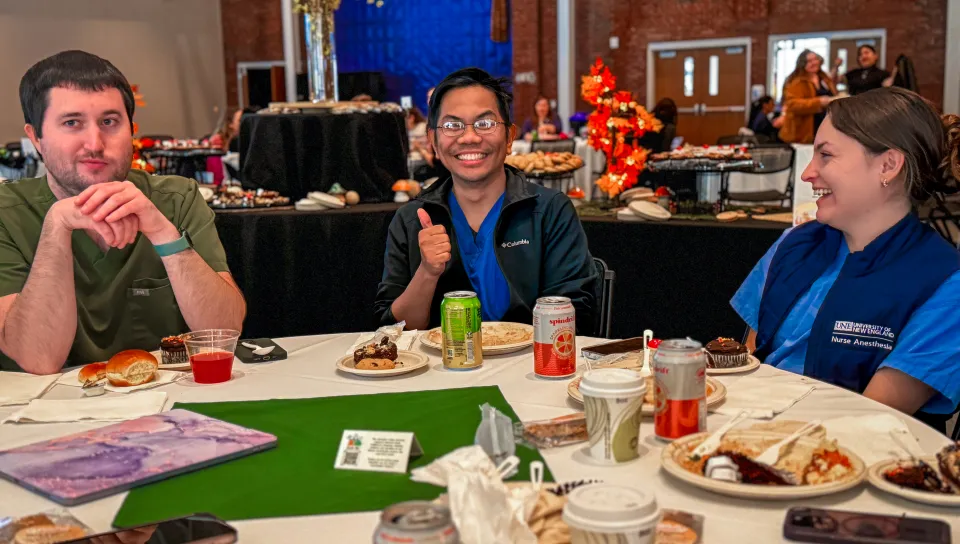 A nurse anesthesia student gives a 'thumbs up' at the lunch table surrounded by friends