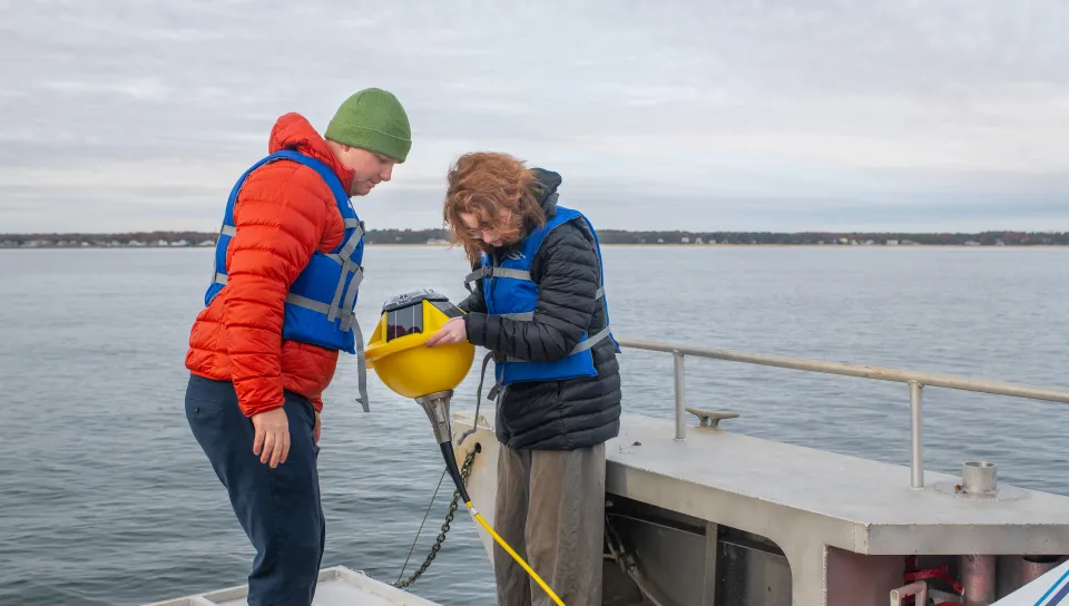 UNE Professor Will Kochtitzky and a student prepare a buoy for deployment off a research boat