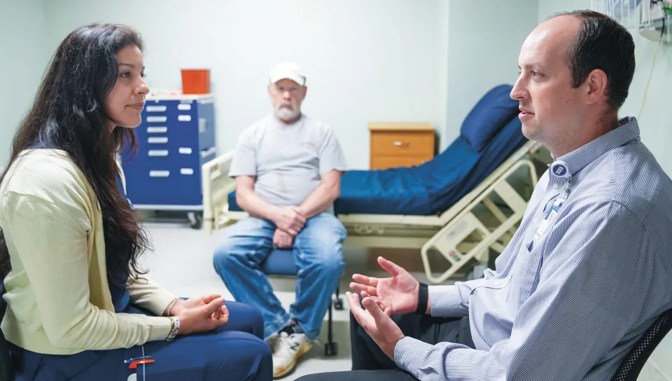Jasmin Gil, a nursing student, sits across from Ben Jones, a College of Dental Medicine student, as they speak with Michael, a patient actor, in a simulated clinical setting.