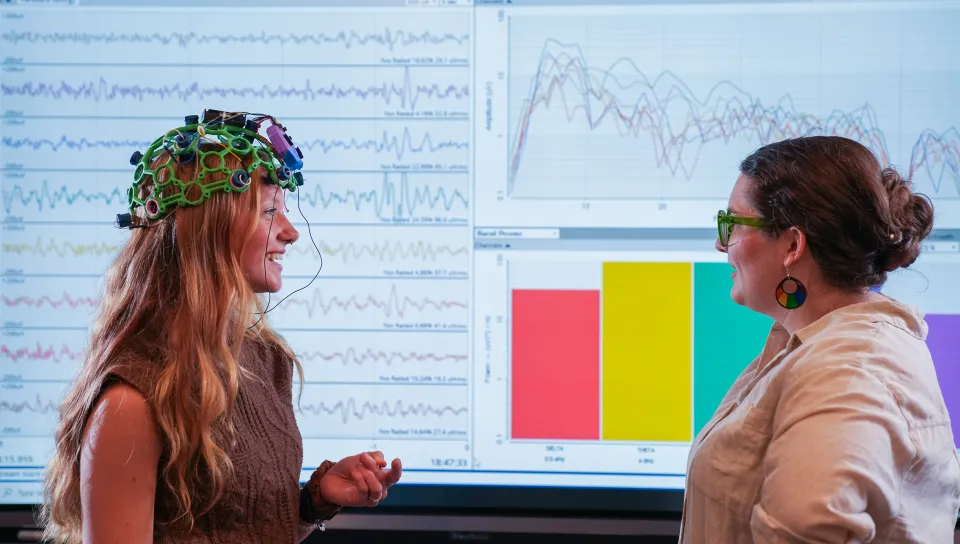 Jessica Howard and Sophia Crockett-Current examining EEG brainwave data and colorful graphs displayed on large monitor.