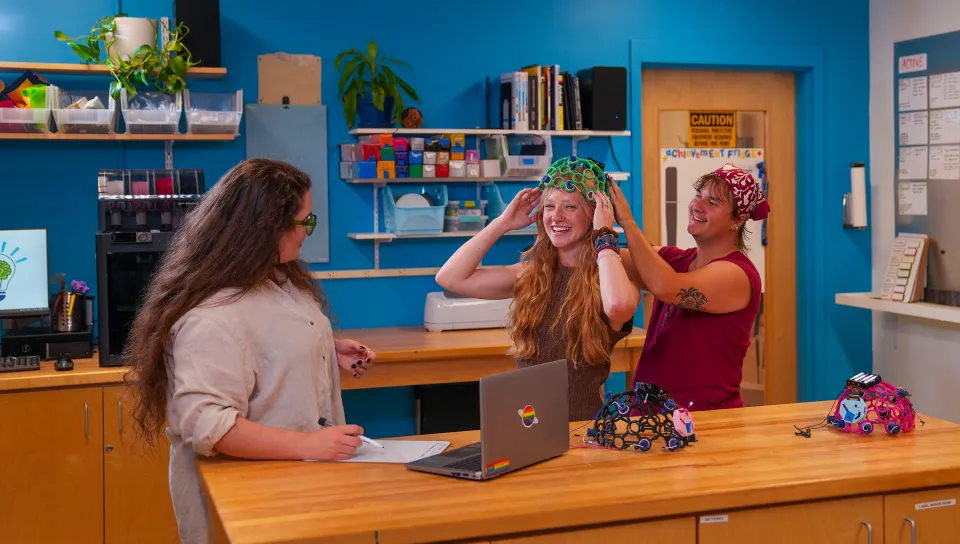 Milo Lypps adjusting a green EEG sensor cap on Jessica Howard in the Makerspace.