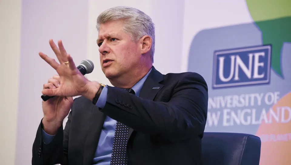 A panelist gestures emphatically with a hand raised while speaking into a microphone during the President's Forum discussion on executive power and democracy